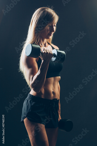 Athletic woman with dumbbells on a dark background
