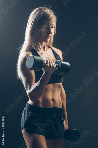 Athletic woman with dumbbells on a dark background © satyrenko