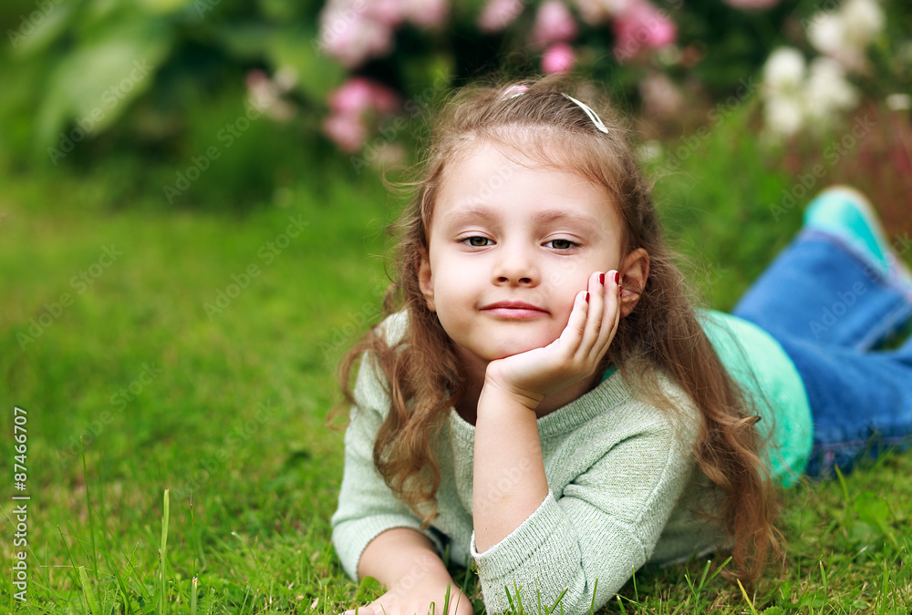 Beautiful long curly hair kid girl lying on green grass in fashi Beautiful long curly hair kid girl lying on green grass in fashi