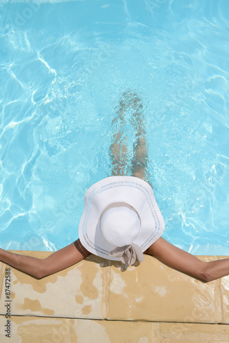 above view of beautiful woman with big white straw hat relaxing in a swimming pool