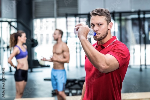 Attentive muscular trainer drinking water