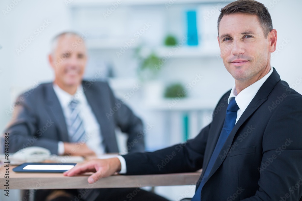 Confident businessman looking at camera with colleague behind Confident businessman looking at camera with colleague behind