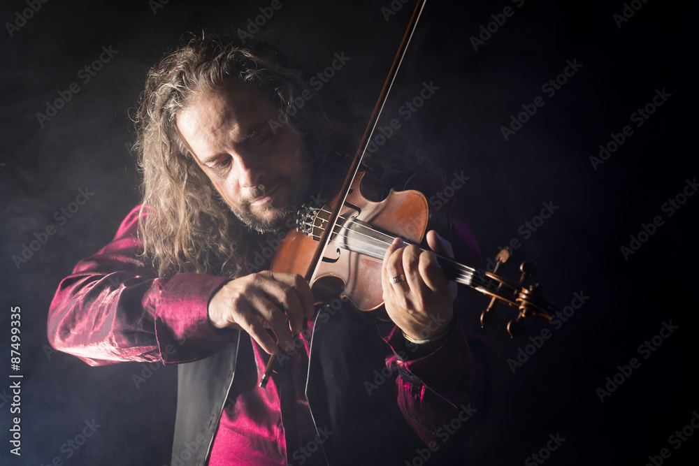 Fototapeta premium handsome man playing classical violin through blue smoke