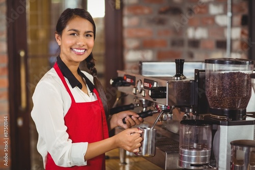 Smiling barista steaming milk at the coffee machine photo