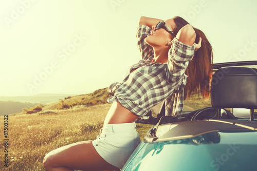 Attractive young woman posing leaning on convertible car at suns