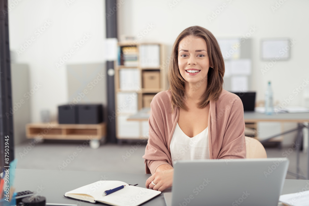 angestellte im büro sitzt lächelnd am schreibtisch