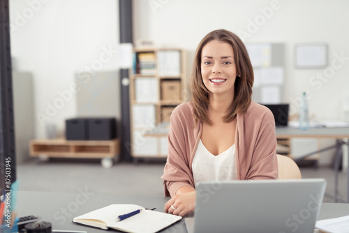 angestellte im büro sitzt lächelnd am schreibtisch © contrastwerkstatt