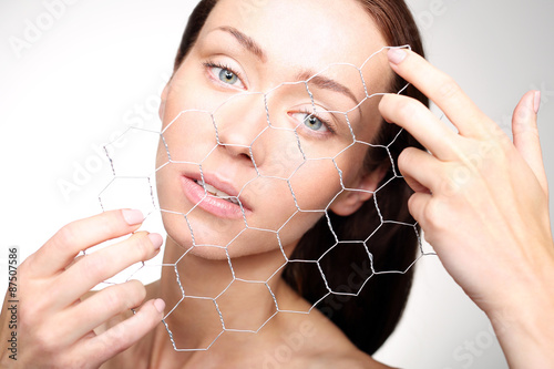 Portret pięknej kobiety rozciągającej przed sobą drucianą siatkę z sześciokątnymi okienkami , symbol budowy komórek skóry