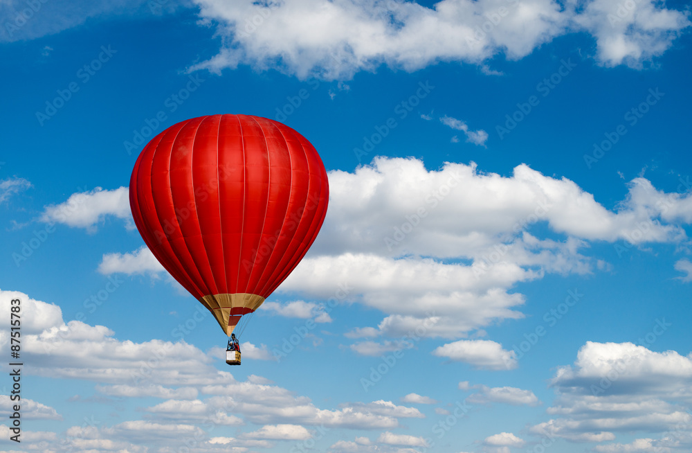 Naklejka premium Red hot air balloon in blue cloudy sky