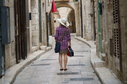 Turista con cappello e borsetta in una vecchia strada di paese