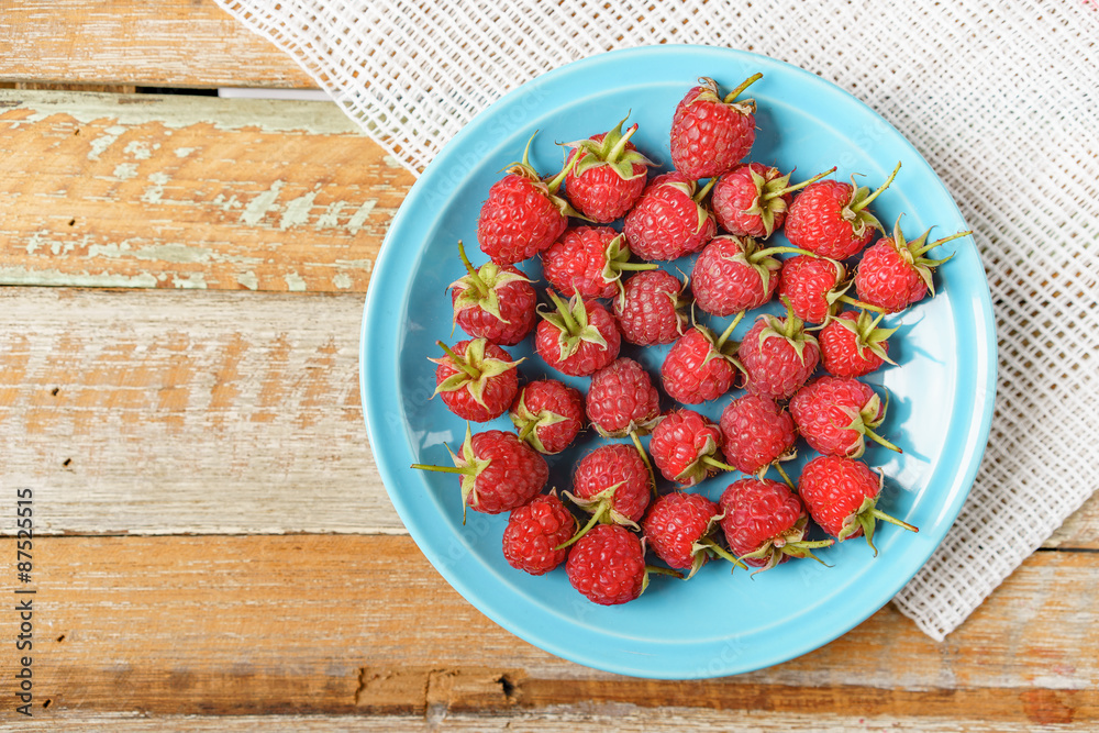 Red rasberry in blue dish and in front of white fabric on old vi Red rasberry in blue dish and in front of white fabric on old vi