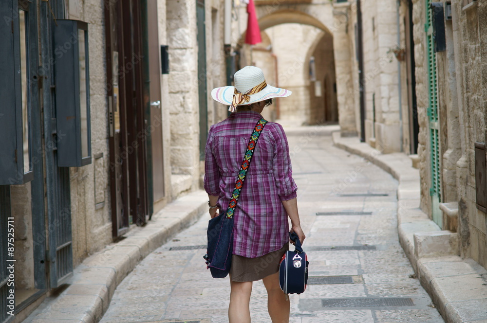 Turista con cappello e borsetta in una vecchia strada di paese