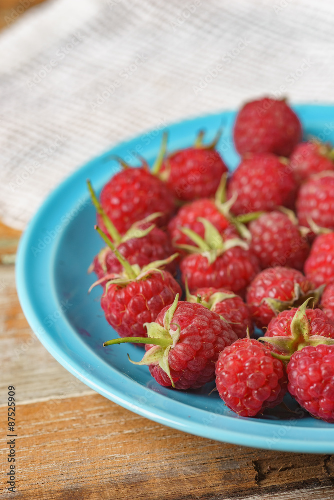Red raspberry in blue dish and in front of white fabric on old v Red raspberry in blue dish and in front of white fabric on old v