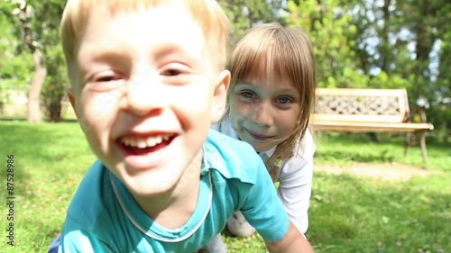 Girl and boy crawls on all fours on the grass in the park and laughs, bark and meow like animals
 photo