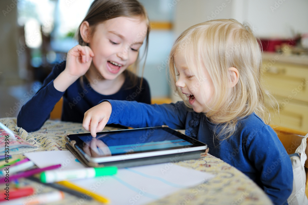 Two little sisters playing with a digital tablet Two little sisters playing with a digital tablet