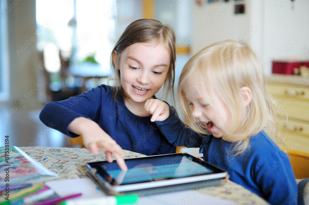 Two little sisters playing with a digital tablet Two little sisters playing with a digital tablet