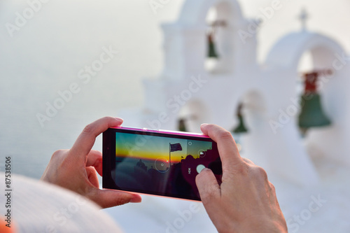 Woman holding a phone taking pictures in Oia Santorini, Greece