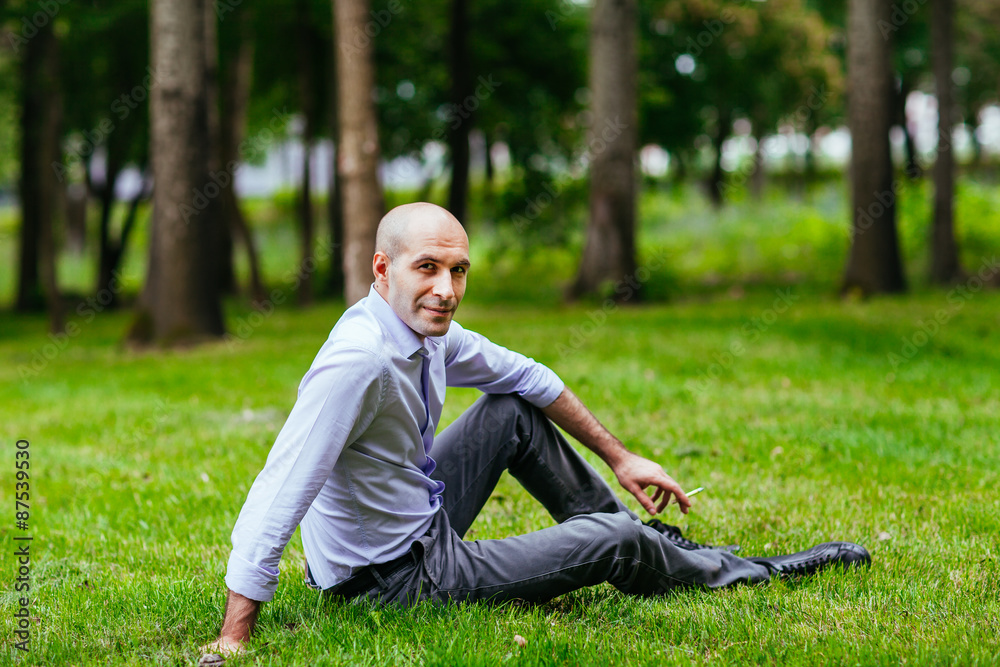 Portrait of a bald and brutal man. Bald guy sitting on the grass Portrait of a bald and brutal man. Bald guy sitting on the grass