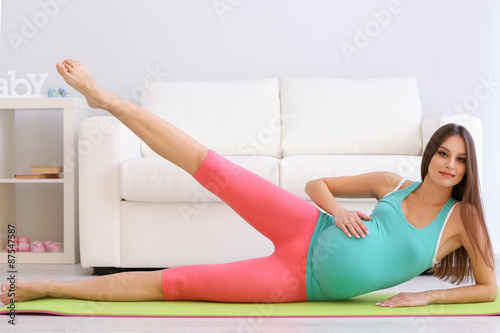 Pregnant woman exercising on green mat in room