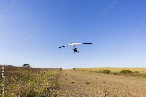 Flying microlight aircraft planes take-off on rural grass airstrip.