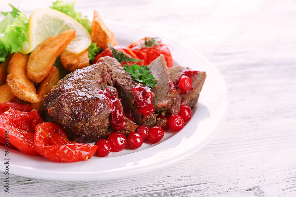 Tasty roasted meat with cranberry sauce and roasted vegetables on plate, on color wooden background Tasty roasted meat with cranberry sauce and roasted vegetables on plate, on color wooden background