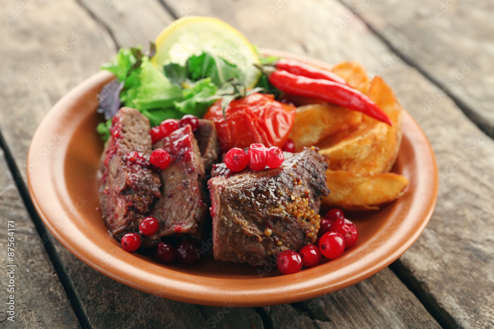 Tasty roasted meat with cranberry sauce, salad and roasted vegetables on plate, on wooden background Tasty roasted meat with cranberry sauce, salad and roasted vegetables on plate, on wooden background