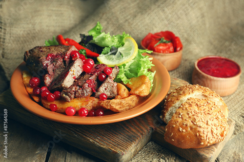 Tasty roasted meat with cranberry sauce, salad and roasted vegetables on plate, on sackcloth background