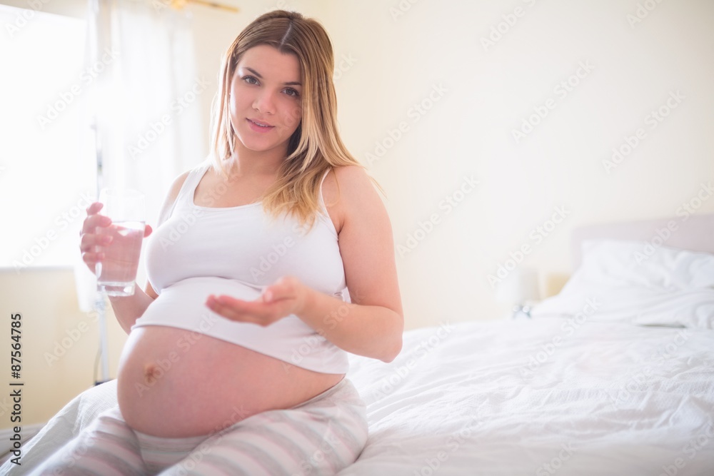 Pregnant woman sitting on bed and holding glass of water Pregnant woman sitting on bed and holding glass of water