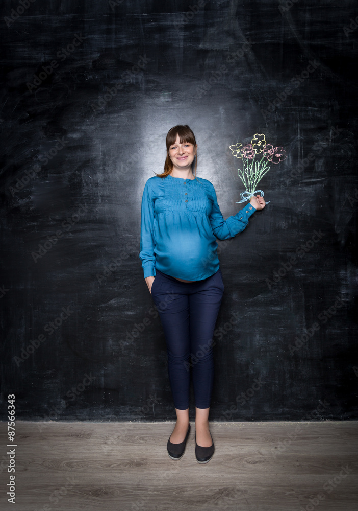 Happy pregnant woman posing with bouquet drawn on big chalkboard