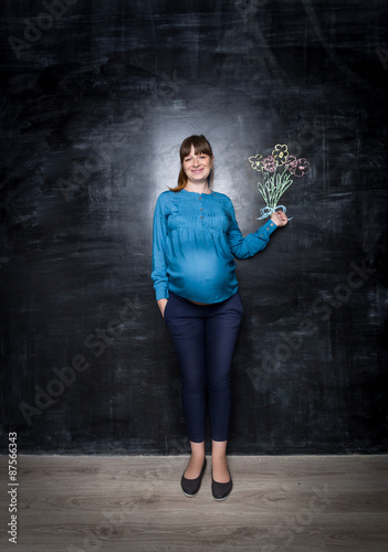 Happy pregnant woman posing with bouquet drawn on big chalkboard