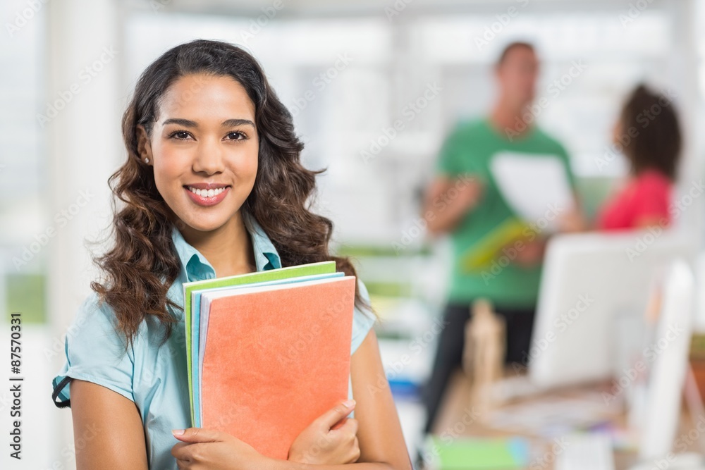 businesswoman holding files with her colleagues behind her businesswoman holding files with her colleagues behind her