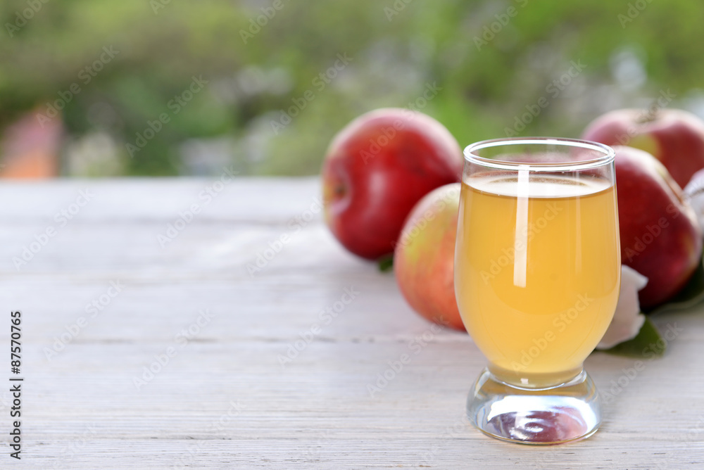 Glass of apple juice and apples on wooden table, on nature background Glass of apple juice and apples on wooden table, on nature background