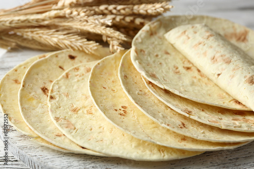 Stack of homemade whole wheat flour tortilla on cutting board, on wooden table background