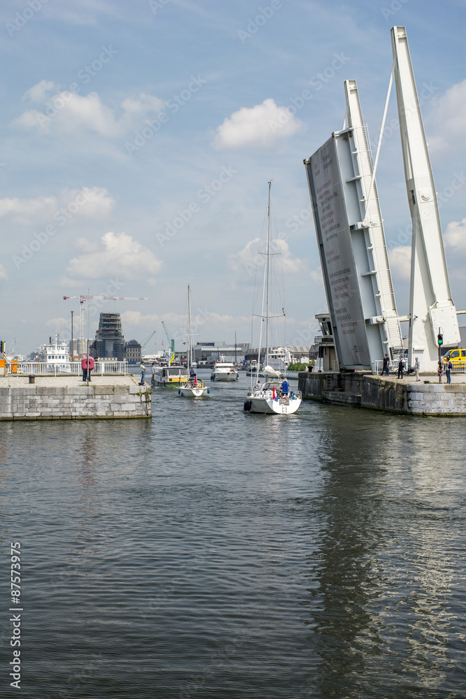 White yachts pass through the gateway under a raised bridge