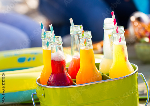 Bottles of lemonade , standing in a colorful green bucket on the