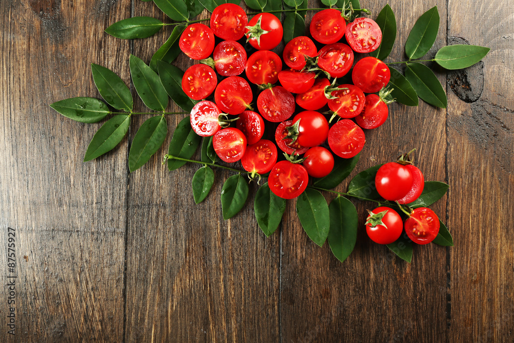 Cherry tomatoes arranged in heart shape with green leaves on wooden background Cherry tomatoes arranged in heart shape with green leaves on wooden background
