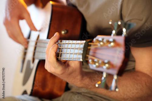 Young man playing on acoustic guitar close up