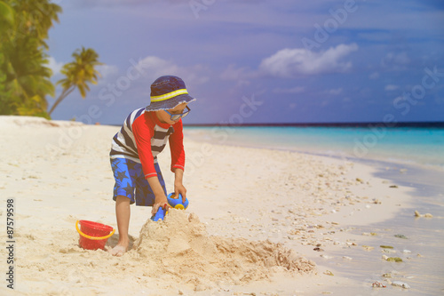 little boy building sandcastle on tropical beach