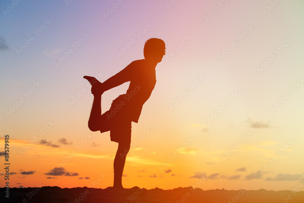 Silhouette of young man doing yoga at sunset