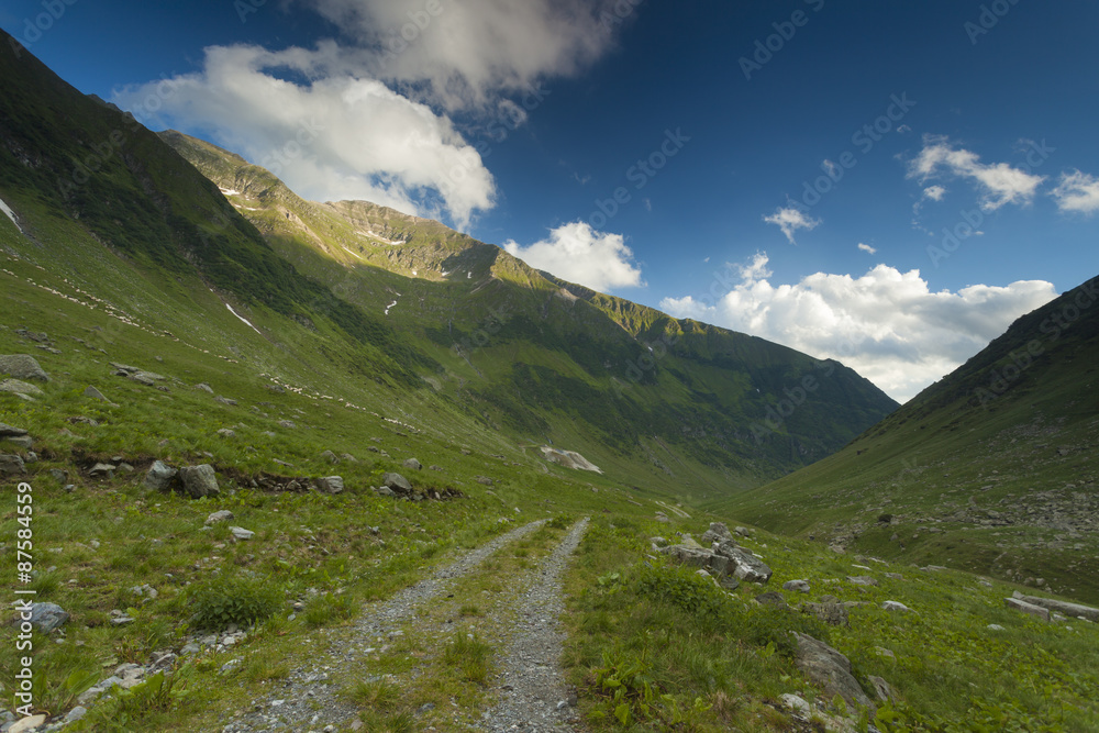 Dirt road in the mountain with blue sky and clouds above