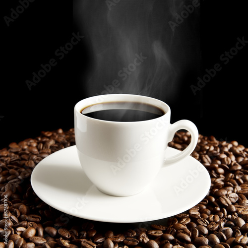 Cup of coffee with haze and coffee beans on black