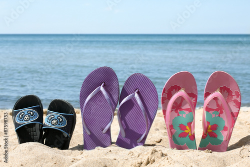 Three pairs of slippers in the sand on a background the blue sea