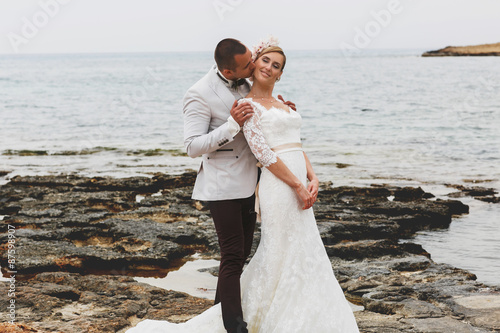 beautiful gorgeous blonde bride and stylish groom kissing, on the background of a sea, wedding ceremony on cyprus.