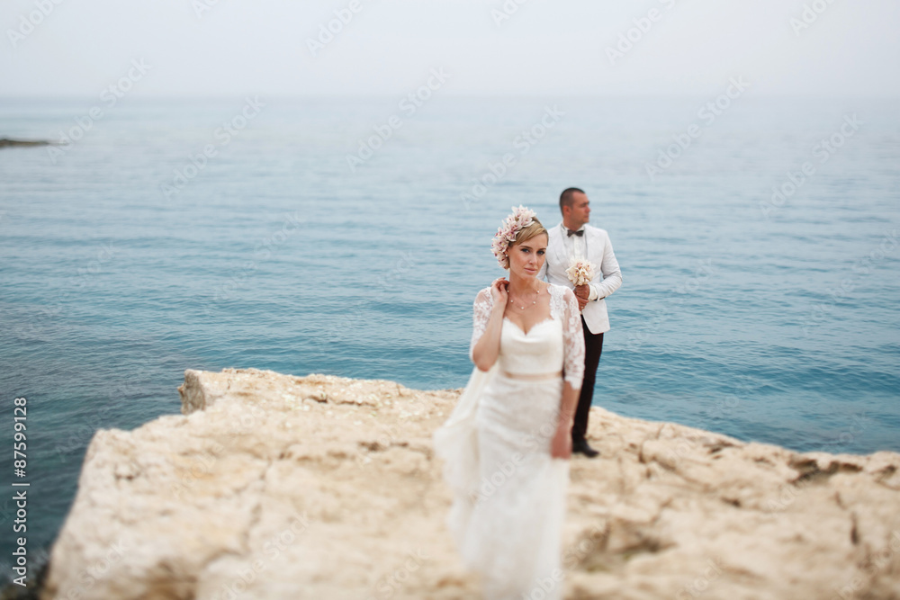 beautiful  gorgeous blonde bride  and stylish groom on rocks, on the background of a sea, wedding ceremony  on cyprus.