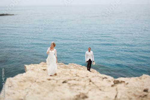 beautiful  gorgeous blonde bride  and stylish groom on rocks  on the background of a sea  wedding ceremony  on cyprus.