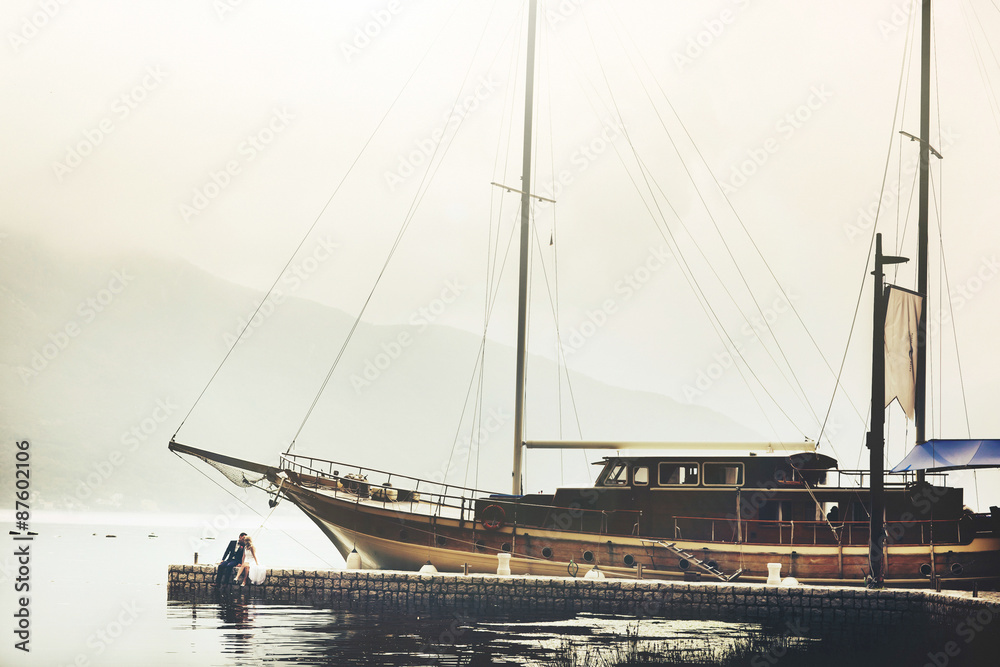 Stylish young bride and groom huging and kissing  on the pier near yacht on background sea and mountains of Montenegro