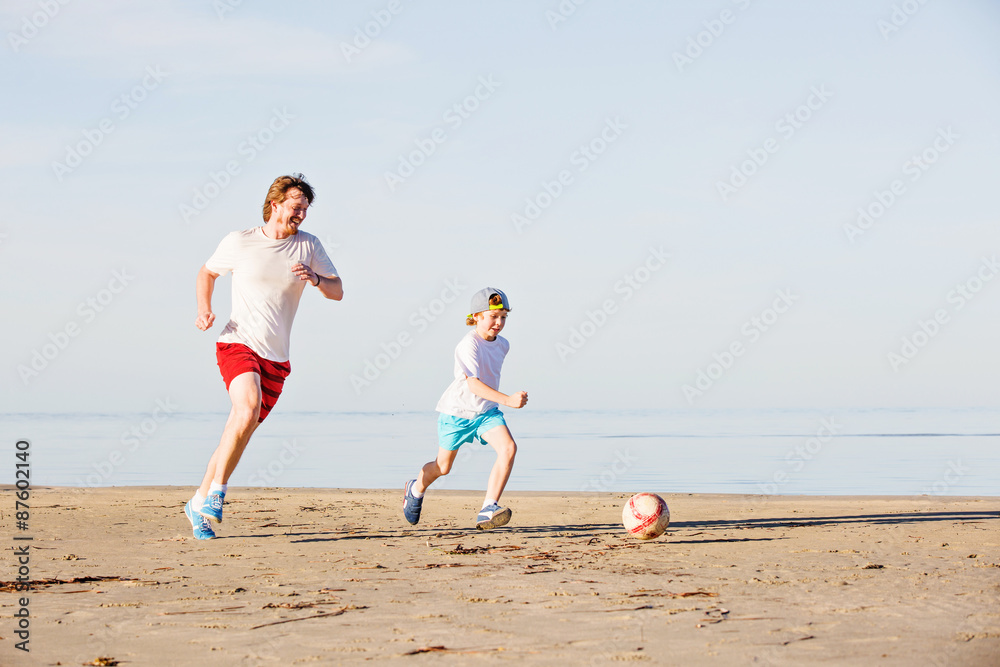 Happy father and son play soccer or football on the beach Happy father and son play soccer or football on the beach