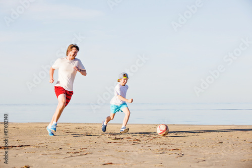 Happy father and son play soccer or football on the beach