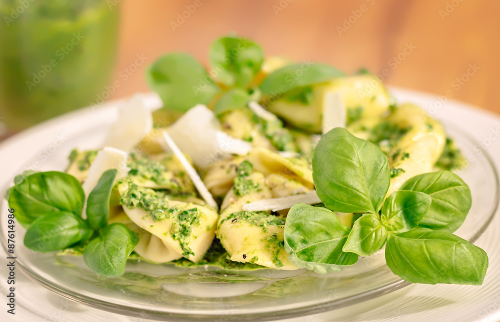Lateral view of a plate of basil ricotta tortelloni with pesto and parmesan flakes.