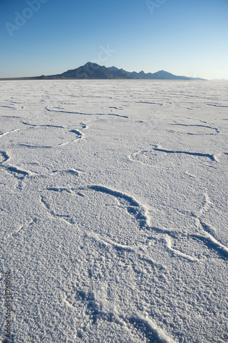 Dramatic white desert background of textured salt formations with rugged mountain range on the horizon